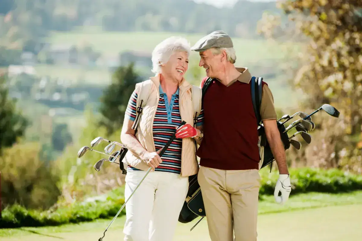 Older couple enjoying a round of golf on a sunny day, smiling and laughing.