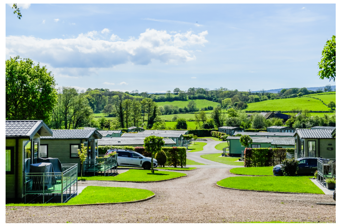 A neat and well-kept holiday park with modern Willerby holiday homes and lodges, surrounded by lush green countryside under a blue summer sky
